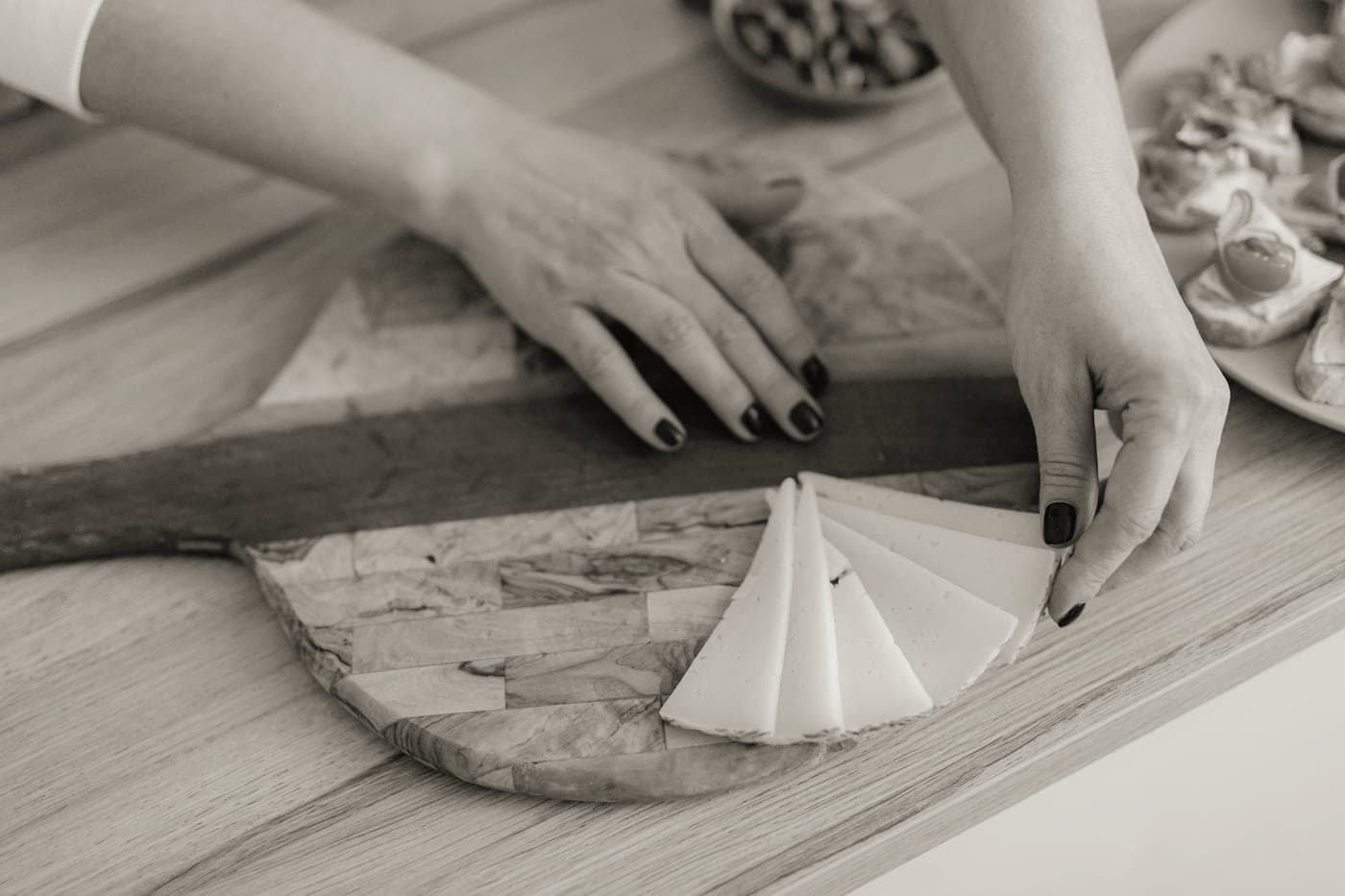 Hands arranging cheese on a wooden board